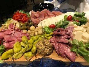 A wooden charcuterie board filled with an assortment of meats, cheeses, pickles, and garnishes.