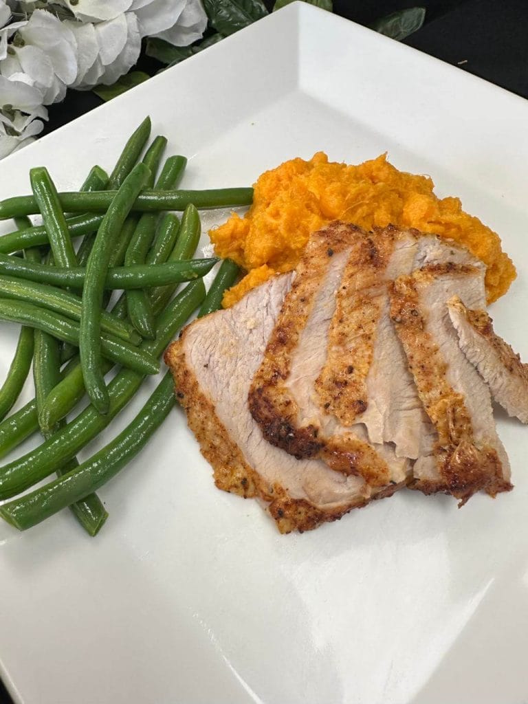 Slices of roasted meat with mashed sweet potatoes and green beans on a white square plate.