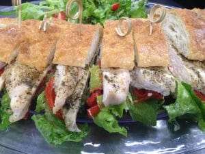 A platter of chicken sandwiches with lettuce and tomato, secured with toothpicks.