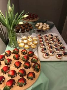 A selection of desserts including chocolate-dipped strawberries, tarts, and mini cupcakes displayed on a table.