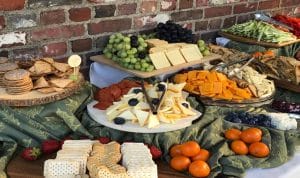 A spread of assorted cheeses, fruits, crackers, and meats on a table with a brick wall in the background.
