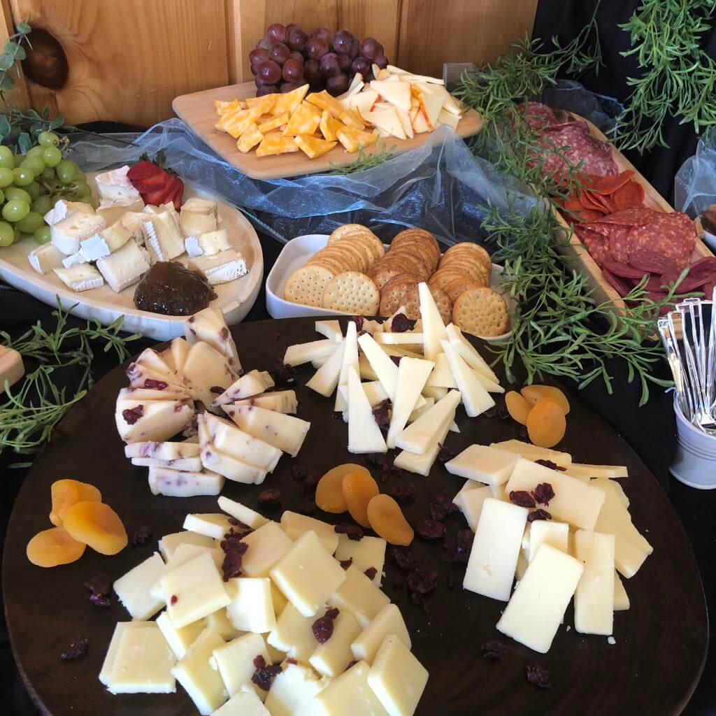 A cheese and charcuterie board featuring a variety of cheeses, grapes, dried fruits, crackers, and cured meats, garnished with herbs.
