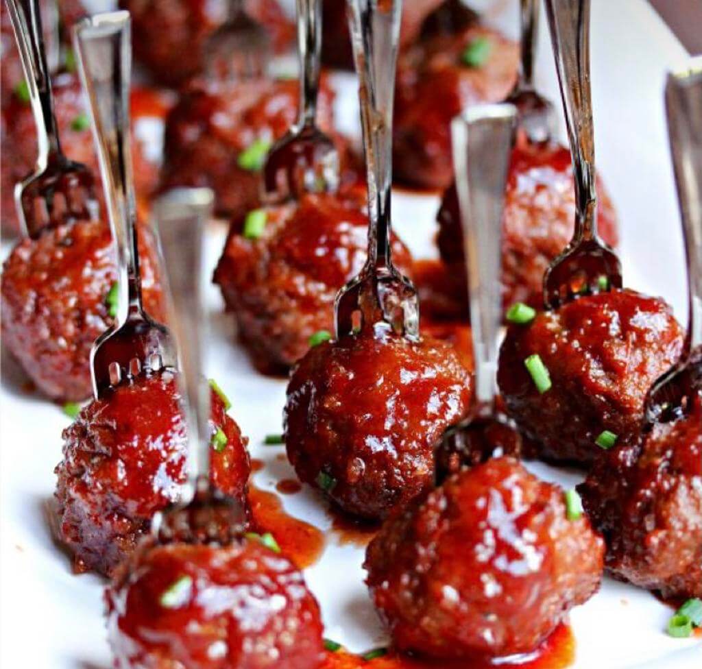 Glazed meatballs served on individual forks with chives garnish, perfect for any event.