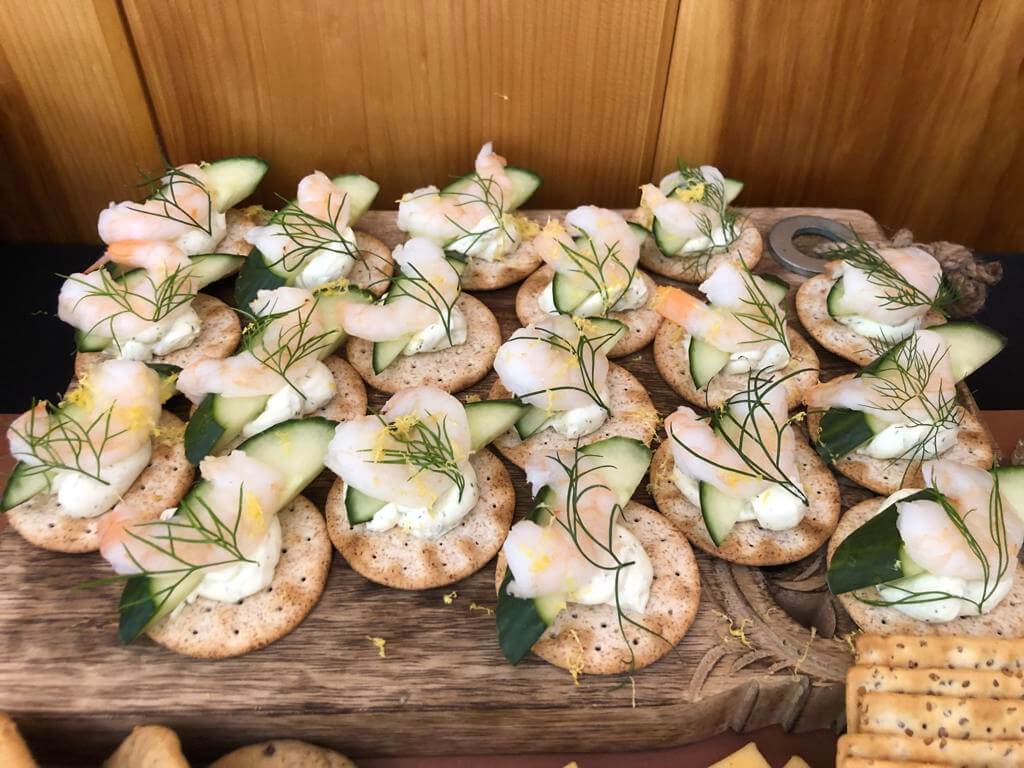 A platter of canapés with shrimp, cucumber, and dill on round crackers.
