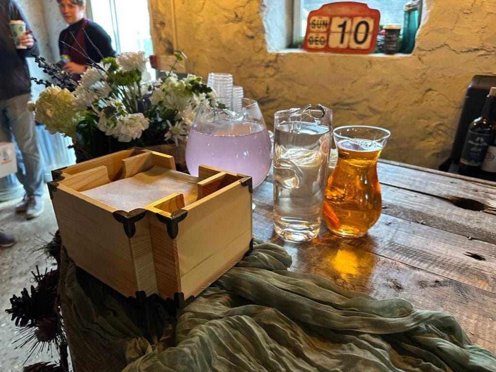 A rustic table setting for an event in Worcester Massachusetts, featuring a wooden box of napkins, a pitcher of pink lemonade, lemon water, and iced tea.