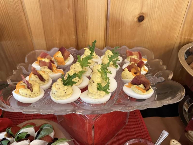 A platter of deviled eggs garnished with bacon and herbs.