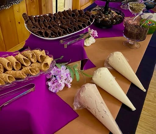 A dessert table with assorted treats, featuring chocolate-dipped cones and pastries on a purple tablecloth, decorated with white floral accents.