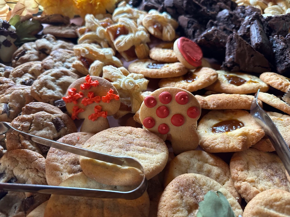 An assortment of freshly baked cookies, including varieties with nuts, chocolate, and fruit fillings, displayed with serving tongs.