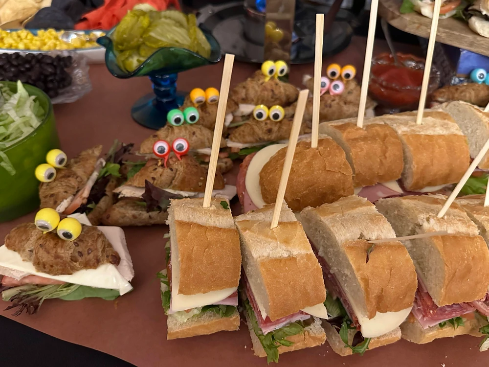 Assorted sandwiches with fun, decorative eyeballs on top displayed on a platter at a party.