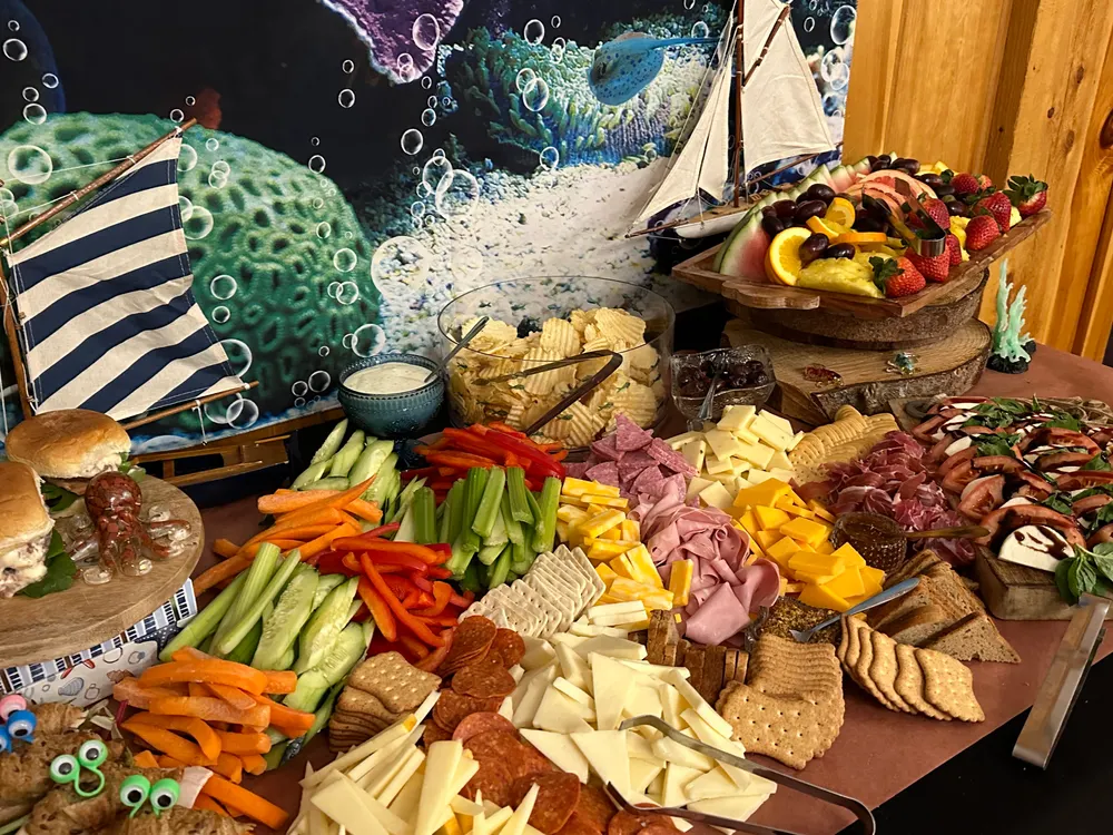 Table with an assortment of food including cheeses, crackers, meats, and fruits, decorated with a nautical theme featuring a model sailboat and octopus elements.