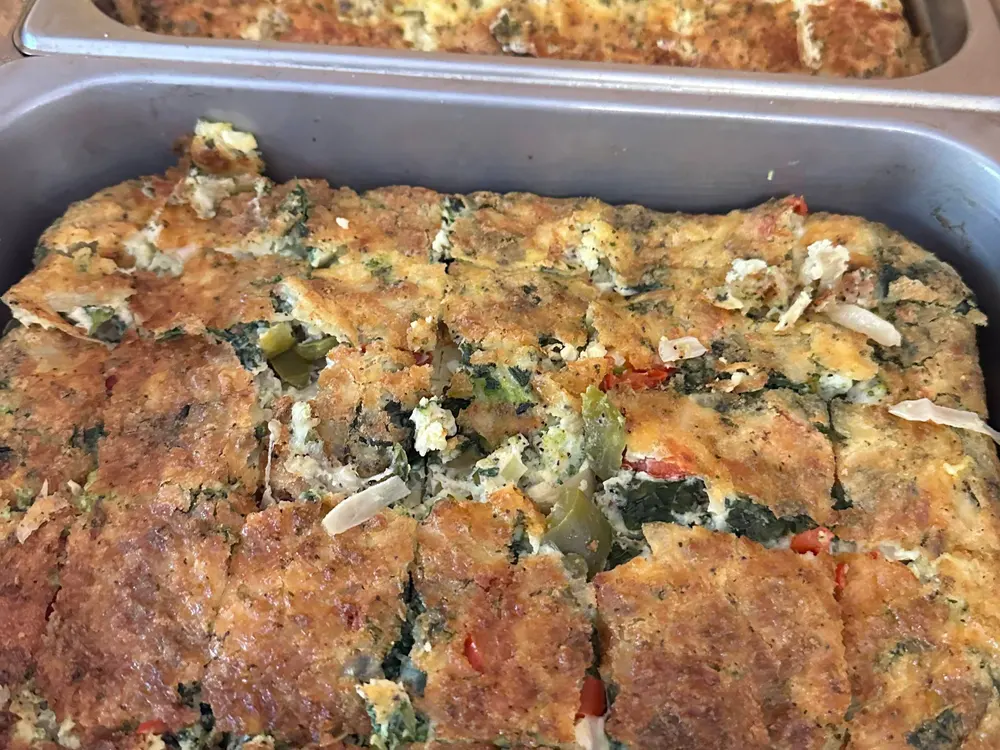 Freshly baked vegetable and cheese casserole in a baking tray, with a golden-brown, crispy top and visible chunks of green broccoli and red peppers.
