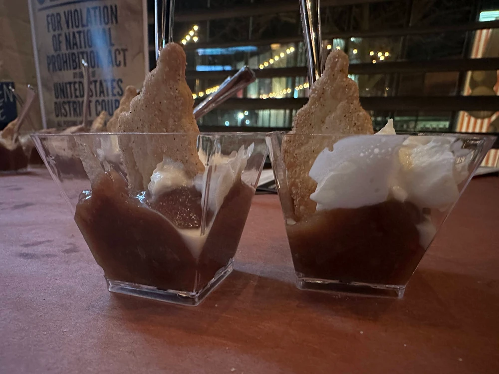 Two cups of dessert featuring layers of cream and a jelly-like substance, served on a wooden counter with a dimly lit background.