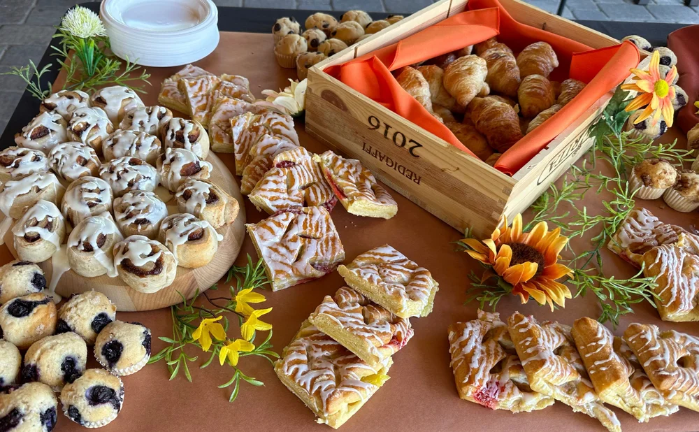 An assortment of pastries displayed on a table, including cinnamon rolls, croissants in a wooden box, and various fruit-filled pastries.