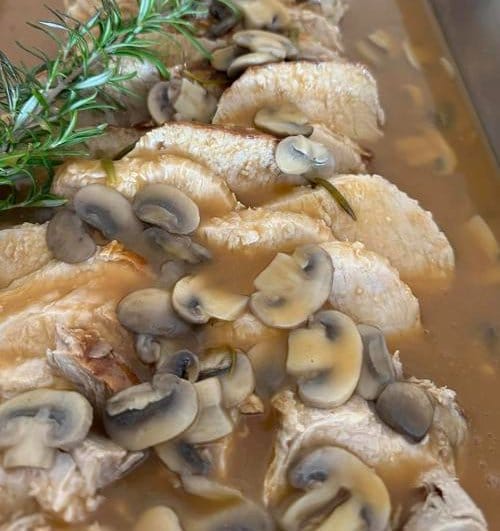 Sliced roasted meat topped with mushroom sauce and garnished with a sprig of rosemary.