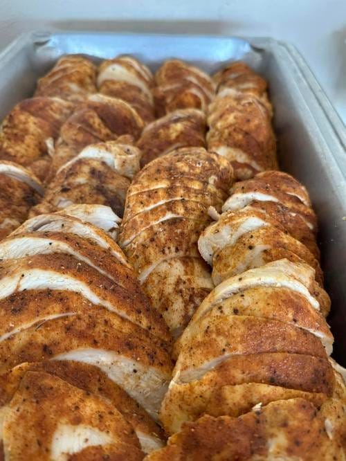 Sliced, seasoned chicken arranged in a catering tray.