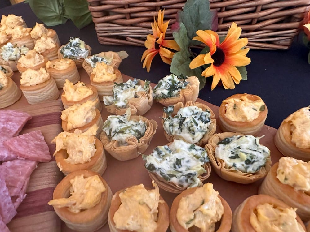 Assorted filled pastry cups with creamy spinach and cheese fillings on a wooden board, accompanied by a basket decorated with artificial flowers.