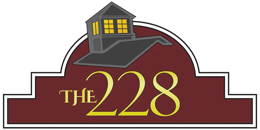 A logo with a maroon background, featuring a house with lit windows above the text "THE 228" in large yellow letters.