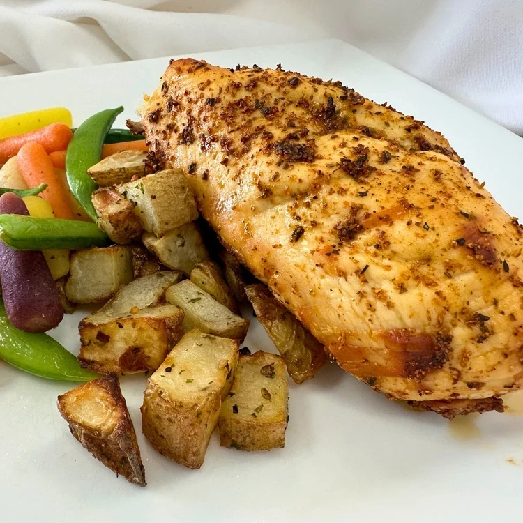 Grilled seasoned chicken breast served with roasted potatoes and a side of mixed vegetables including carrots and snap peas on a white plate.