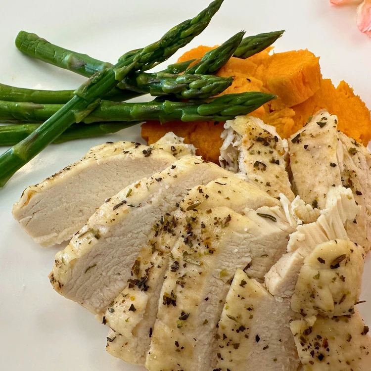 Sliced herb-seasoned chicken breast served with steamed asparagus and mashed sweet potatoes on a white plate.