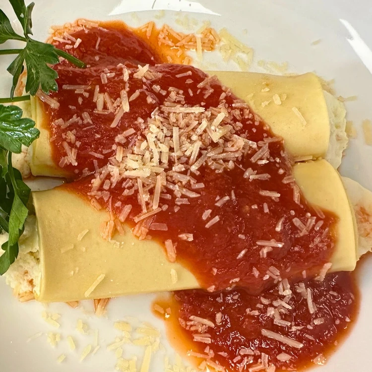 Two stuffed pasta rolls topped with tomato sauce and grated cheese, garnished with a sprig of parsley on a white plate.