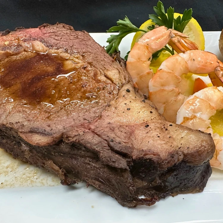 A slice of prime rib served with shrimp, garnished with parsley and lemon on a white plate.